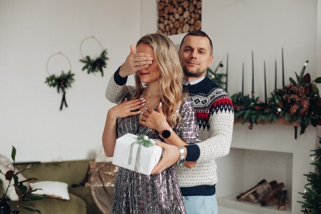 Hübscher junger Mann, der Hand über Augen seiner Freundin hält, während er ihr ein besonderes Weihnachtsgeschenk gibt