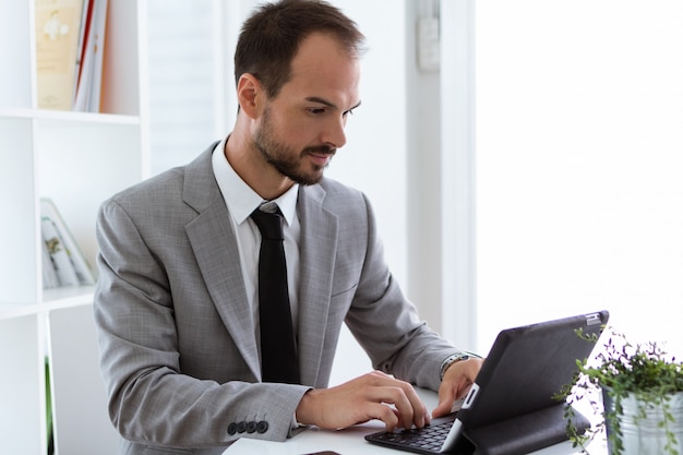 Hübscher junger Mann, der mit digitaler Tablette im Büro arbeitet.