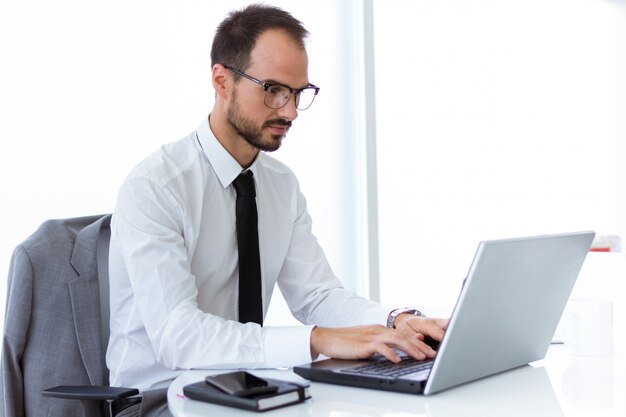 Hübscher junger Mann, der mit Laptop im Büro arbeitet.