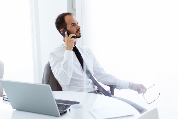 Hübscher junger Mann, der mit Laptop und Handy im Büro arbeitet.