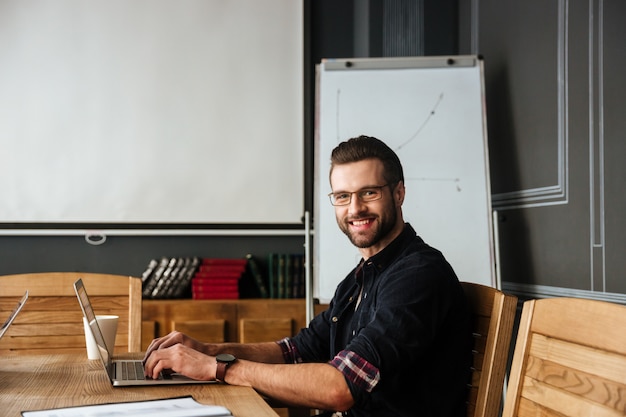 Hübscher junger Mann, der nahe Kaffee während der Arbeit sitzt