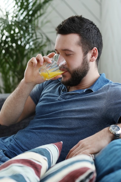 Hübscher junger Mann, der Orangensaft zu Hause trinkt