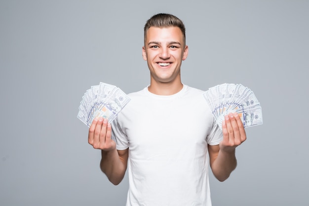 Hübscher junger Mann im weißen T-Shirt halten viele Dollarnoten in seinen Händen lokalisiert auf weißem Hintergrund