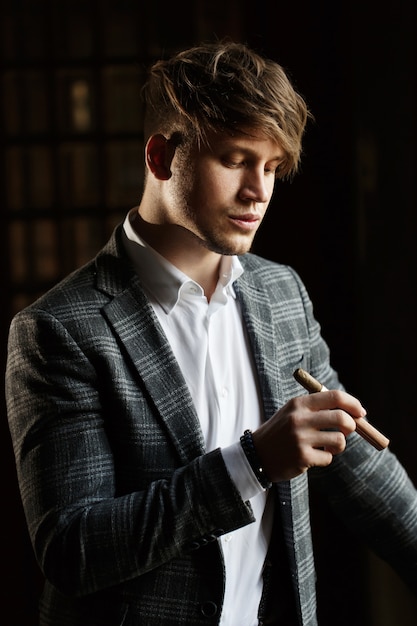 Hübscher junger Mann in der grauen Klage steht mit einer Zigarre