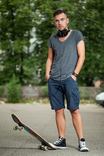 Hübscher Kerl mit Kopfhörern und Skateboard
