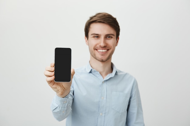 Hübscher lächelnder Mann, der Smartphonebildschirm zeigt