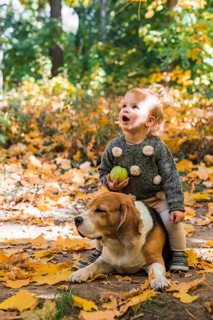 Hübscher Mädchenholdingball, der auf ihrem Haustierspürhundhund im Wald sitzt