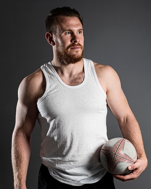 Hübscher männlicher Rugbyspieler, der Ball neben Hüfte hält