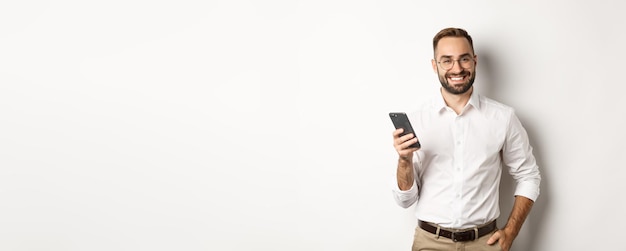 Hübscher Manager, der Smartphone verwendet und zufrieden lächelt, indem er eine Textnachricht sendet, die über weißem Hintergrund steht