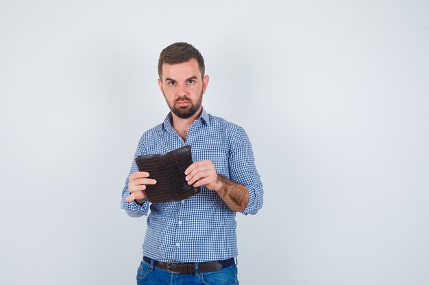 Hübscher Mann, der Brieftasche im Hemd, in den Jeans hält und ernst schaut, Vorderansicht.