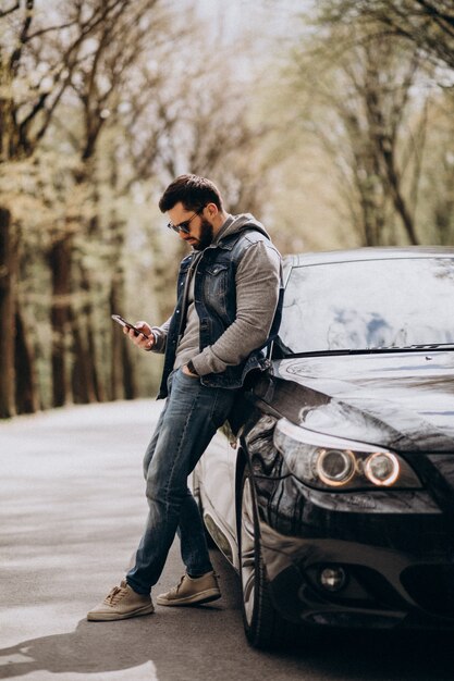 Hübscher Mann, der durch das Auto im Park steht