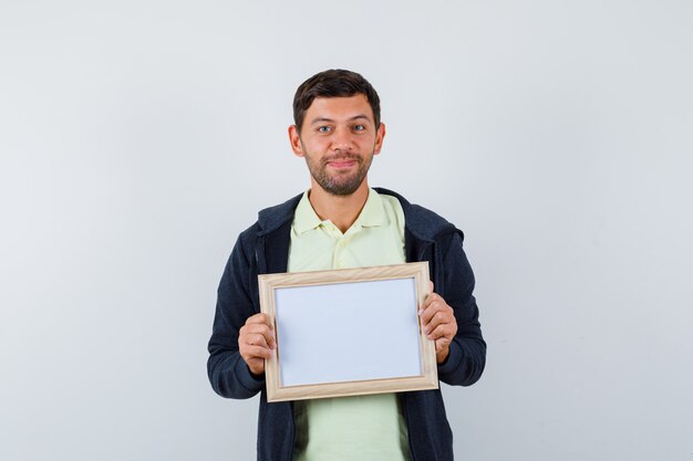 Hübscher Mann, der einen Fotorahmen in einem lässigen Outfit hält