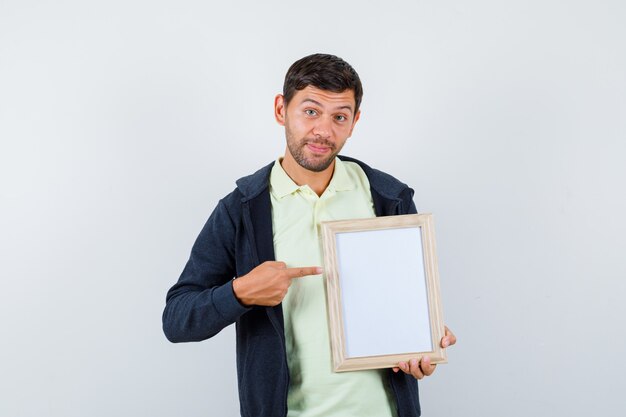 Hübscher Mann, der einen Fotorahmen in einem lässigen Outfit hält