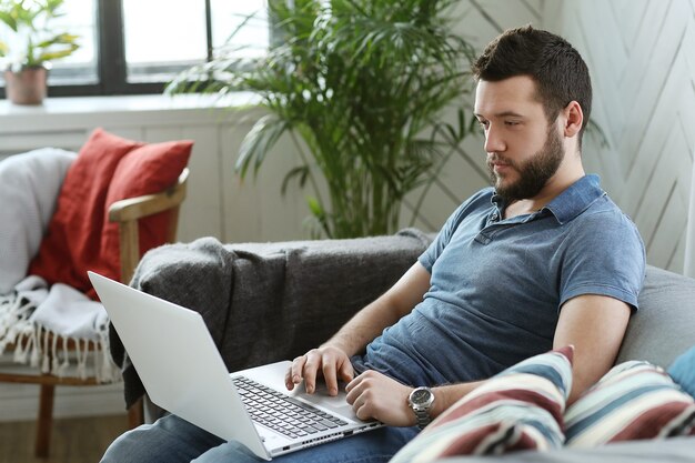 Hübscher Mann, der Laptop zu Hause benutzt. Telearbeitskonzept