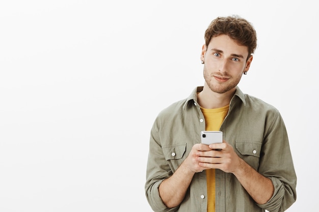 Hübscher Mann, der mit Smartphone im Studio aufwirft