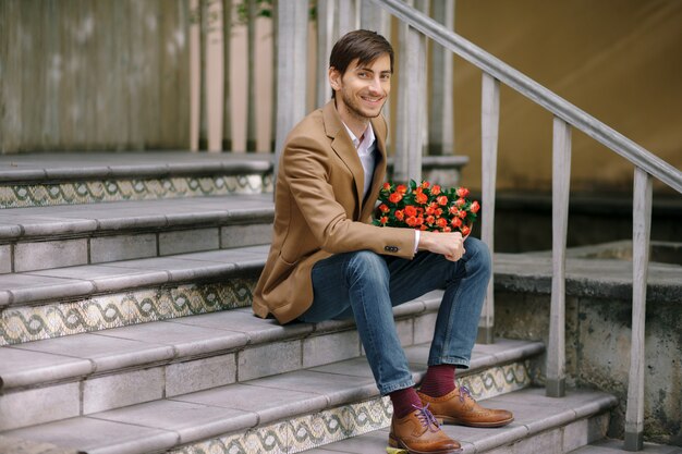 Hübscher Mann, der Strauß der Rosen hält, die glücklich lächeln