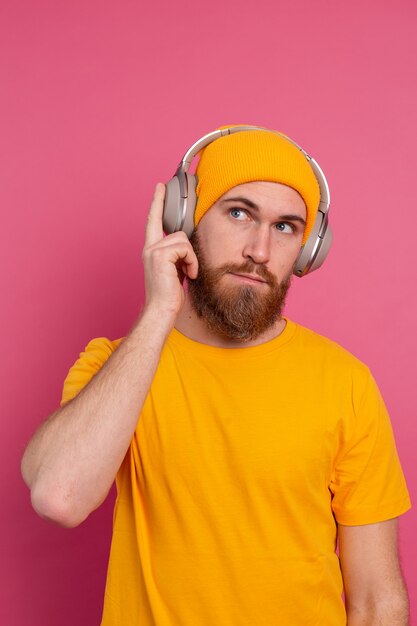 Hübscher Mann im lässigen Hören der Musik mit Kopfhörern lokalisiert auf rosa Hintergrund