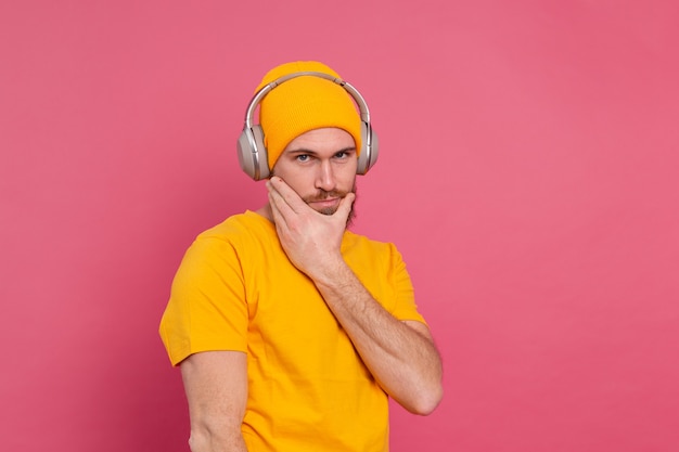 Hübscher Mann im lässigen Hören der Musik mit Kopfhörern lokalisiert auf rosa Hintergrund