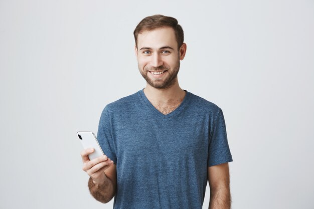 Hübscher Mann im lässigen T-Shirt unter Verwendung des Mobiltelefons
