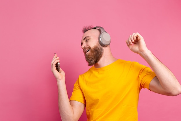 Hübscher Mann im lässigen Tanzen mit Handy und Kopfhörern lokalisiert auf rosa Hintergrund