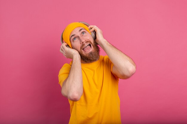 Hübscher Mann im lässigen Tanzen mit Kopfhörern lokalisiert auf rosa Hintergrund