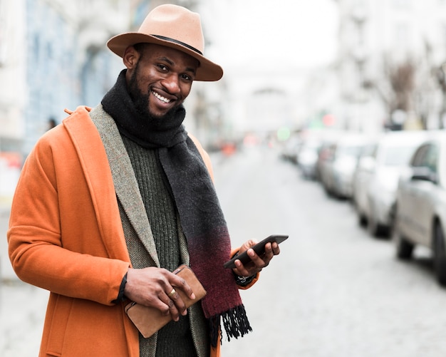 Hübscher Mann in der orange Jacke, die sein Telefon hält