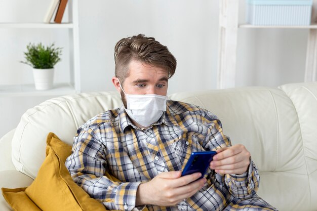 Hübscher Mann mit Gesichtsmaske, die Telefon hält