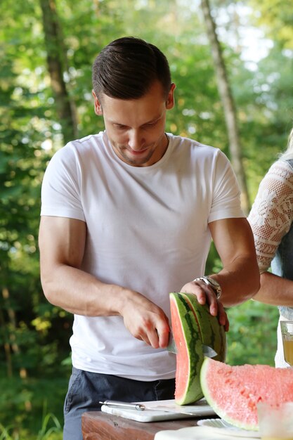 Hübscher Mann mit weißem T-Shirt, das Wassermelone schneidet