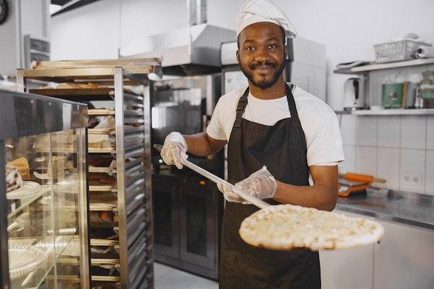 Hübscher Pizzaiolo, der Pizza in der Küche in der Pizzeria macht. Afroamerikanische Ethnizität.