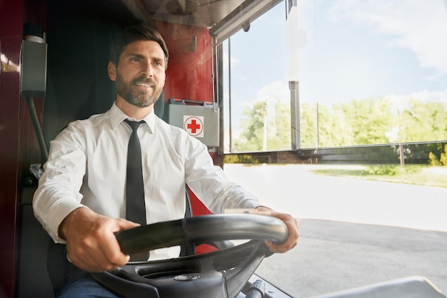 Kostenloses Foto hübscher, professioneller busfahrer, der am lenkrad in der kabine bei der arbeit sitzt und lächelt