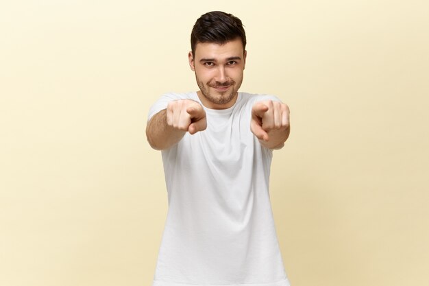 Hübscher selbstbewusster positiver junger Mann im weißen lässigen T-Shirt, das nach vorne zeigt