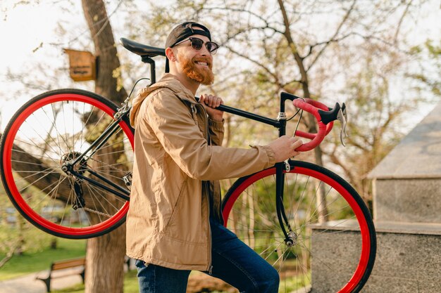 Hübscher stilvoller bärtiger Hipster-Mann in der Jacke und in der Sonnenbrille, die allein in der Straße mit Rucksack auf Fahrrad reisen Gesunder aktiver Lebensstil reisender Rucksacktourist