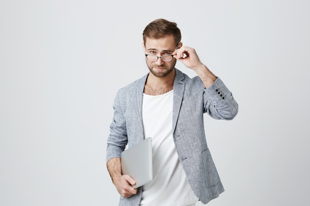 Hübscher stilvoller männlicher Unternehmer in Gläsern mit Laptop