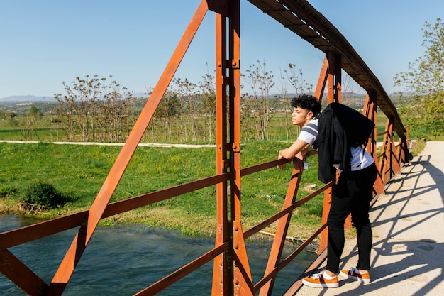 Hübscher stilvoller Mann, der auf Brücke über schönem Fluss steht