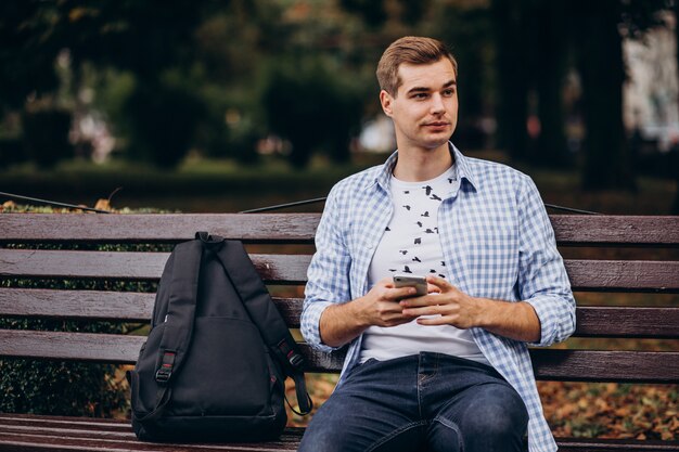 Hübscher Student, der auf Bank sitzt und Telefon benutzt