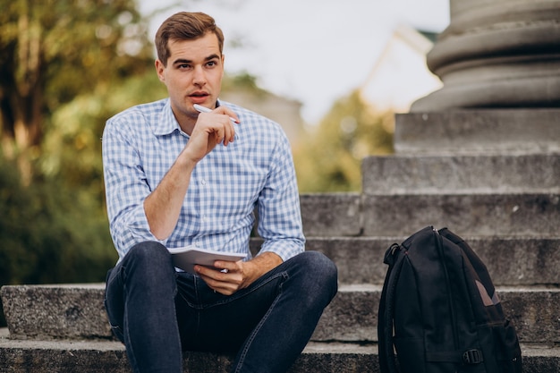 Hübscher Student, der auf Treppen der Universität sitzt und studiert