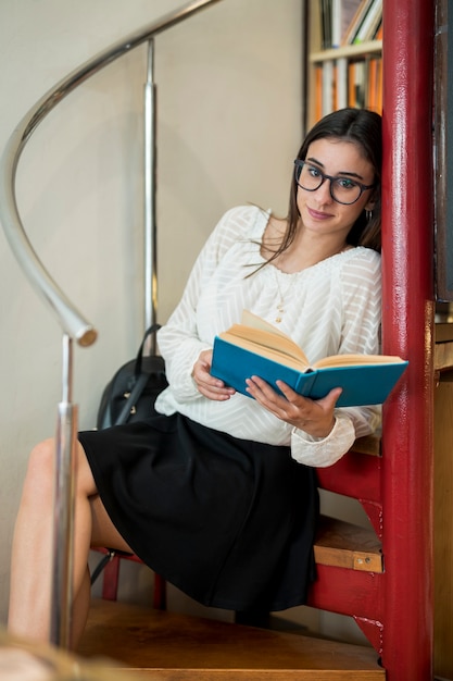 Hübscher Student mit dem Buch, das auf Treppen sitzt