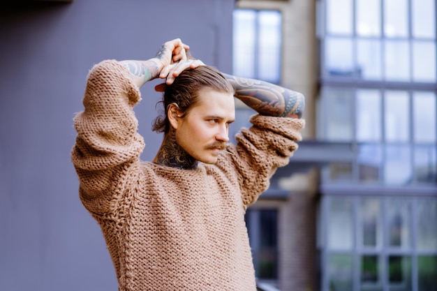 Kostenloses Foto hübscher tätowierter sexy mann mit langen haaren und schnurrbart in einem strickpullover. porträt außerhalb nahaufnahme.