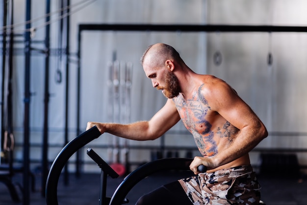 Kostenloses Foto hübscher tätowierter starker mann im fitnessstudio, der cardio tut