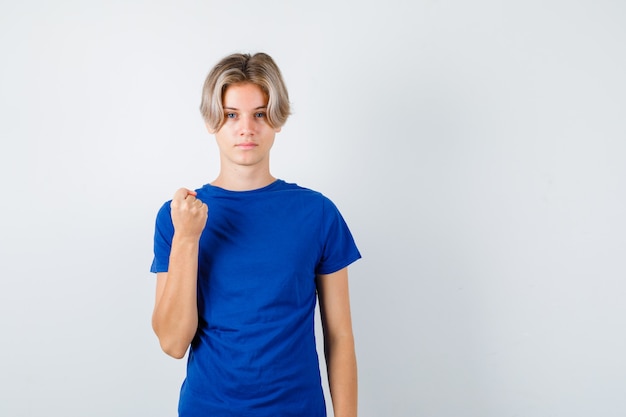 Hübscher Teenager, der geballte Faust im blauen T-Shirt zeigt und stolz aussieht. Vorderansicht.