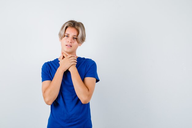 Hübscher Teenager, der im blauen T-Shirt unter Halsschmerzen leidet und belästigt aussieht. Vorderansicht.