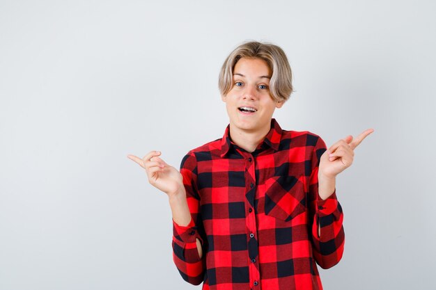 Hübscher Teenager, der im karierten Hemd nach rechts und links zeigt und fröhlich aussieht. Vorderansicht.