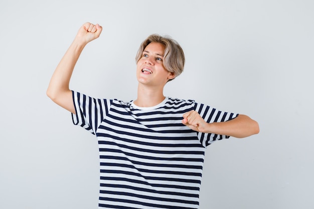 Hübscher Teenager, der Siegergeste im gestreiften T-Shirt zeigt und glücklich aussieht, Vorderansicht.