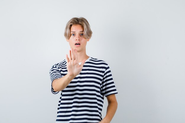 Hübscher Teenager im gestreiften T-Shirt mit Stoppgeste und verängstigtem Blick, Vorderansicht.