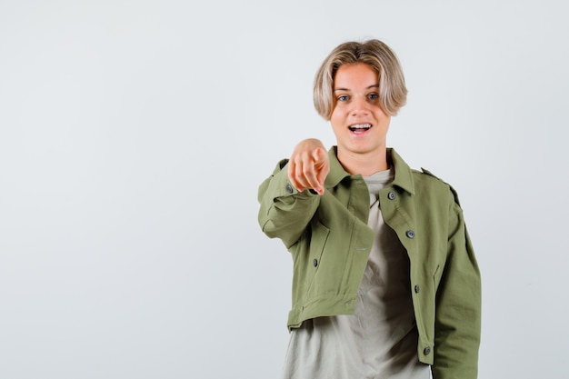Hübscher Teenager in grüner Jacke, der auf die Kamera zeigt und fröhlich aussieht