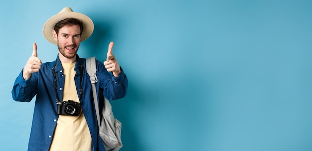 Kostenloses Foto hübscher tourist, der in den sommerurlaub geht, mit kamera und rucksack, der mit dem finger auf die kamera und hinein zeigt