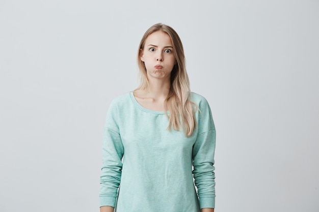 Hübsches blondes europäisches weibliches Model mit abgerundeten Lippen, sieht erstaunt aus, hat verwirrten Ausdruck, drückt ihre Gefühle aus