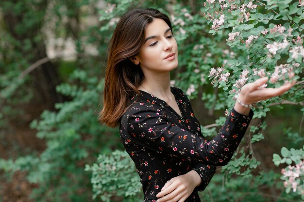 Hübsches junges Modell mit Fotoshooting im blühenden Garten, das Blütenbewunderung berührt