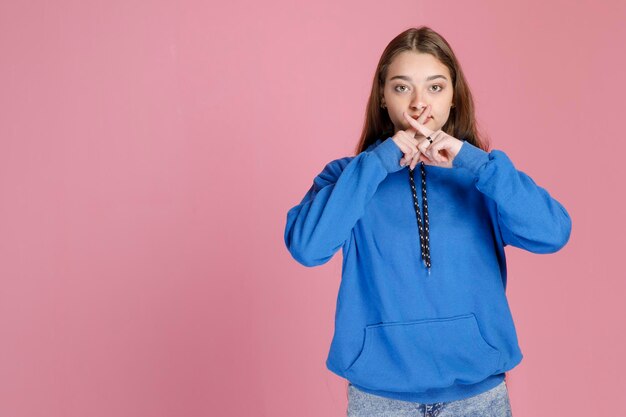 Hübsches kaukasisches Mädchen in lässigem Outfit, das die Zeigefinger am Mund kreuzt und eine ablehnende Geste zeigt