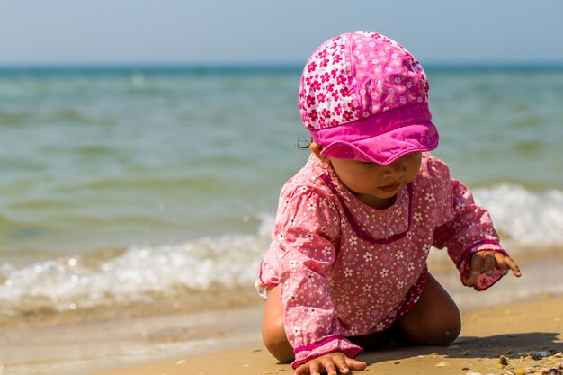 hübsches kleines Mädchen, das am Strand krabbelt, das freudige Kind, Gefühle